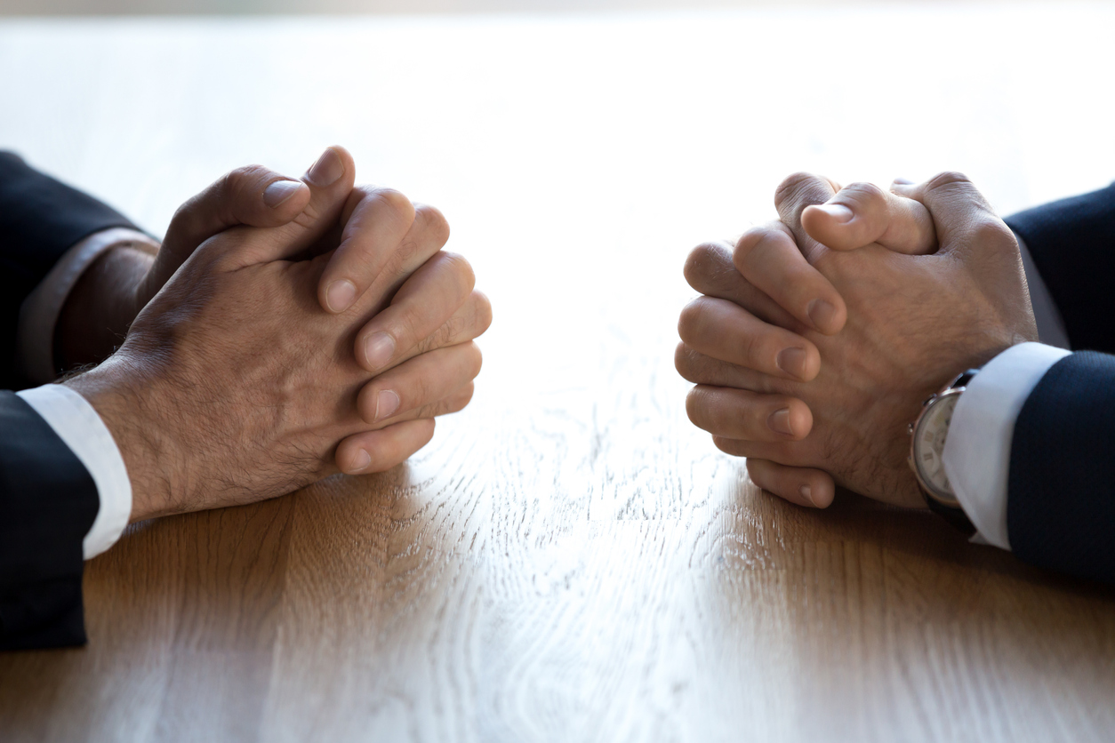 Two pairs of clasped hands on desk
